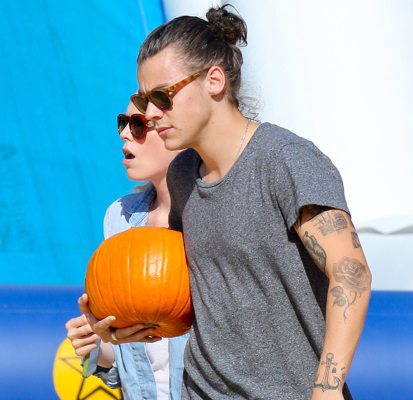 Harry Styles de manbun e óculos escuros, carregando uma abóbora.